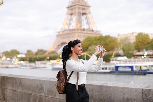 Young woman standing on embankment in Paris and watching photos