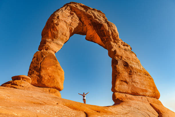 Young woman standing under Delicate Arch in Arches National Park, Utah, USA Young woman standing under Delicate Arch in Arches National Park, Utah, USA,Nikon D3x arches national park stock pictures, royalty-free photos & images