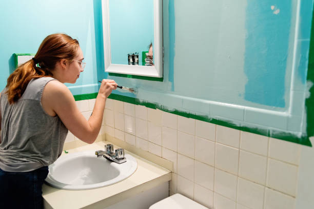 Young woman step by step DIY in home small bathroom. Young woman doing step by step DIY in small appartement bathroom. Here she is starting painting the wall a lighter blue. Horizontal waist up indoors shot with copy space. bathroom painting stock pictures, royalty-free photos & images