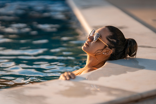 Young woman sunbathing in the pool at sunset