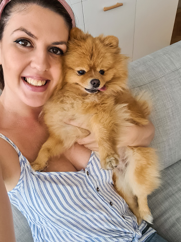 Beautiful young woman lying on the sofa and taking a selfie with her cute dog. Her POV.