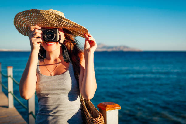 Young woman traveler taking photos of sea landscape on pier using camera. Summer vacation in Egypt stock photo