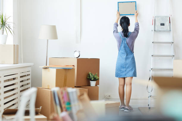 Young Woman Unpacking Boxes in New Home Full length back view portrait of young Asian woman decorating new home while moving in to new house or apartment, copy space college dorm stock pictures, royalty-free photos & images