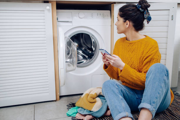 Young woman using a mobile app to adjust her smart washing machine stock photo