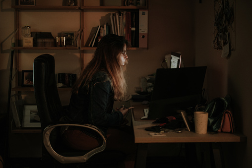 Side view of a young woman using computers in a dark room / office