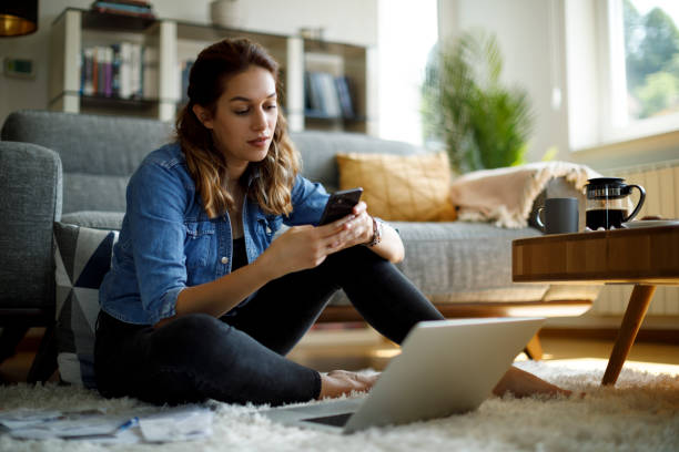 Young woman using mobile phone and laptop at home stock photo