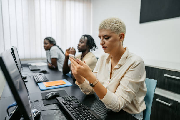 Young Woman Using Phone In A Programing Class Profile of a beautiful young woman sitting in a programing class and using smart phone. associate degree stock pictures, royalty-free photos & images