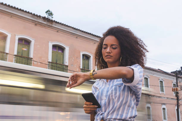 jonge vrouw te wachten op een taxi besteld via mobiele app in de stad in de rush hour - woman horloge stockfoto's en -beelden