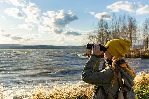 Young woman watching birds with binocular on lake. Scientific research