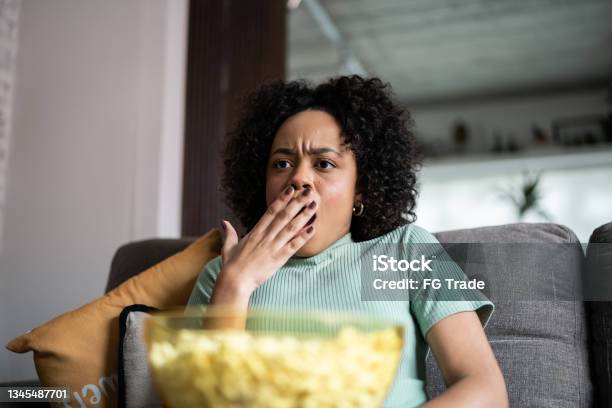 Young woman watching TV and eating popcorn at home