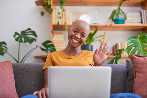A young woman waves hello during a remote call on her laptop from home stock photo