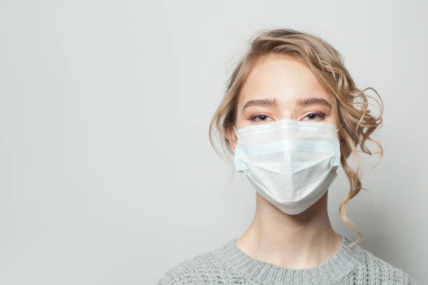 ung kvinna klädd i en ansiktsmask på grå bakgrund. influensaepidemi och virusskyddskoncept - face mask bildbanksfoton och bilder