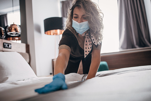 Young woman wearing protective face mask and gloves while working at a hotel