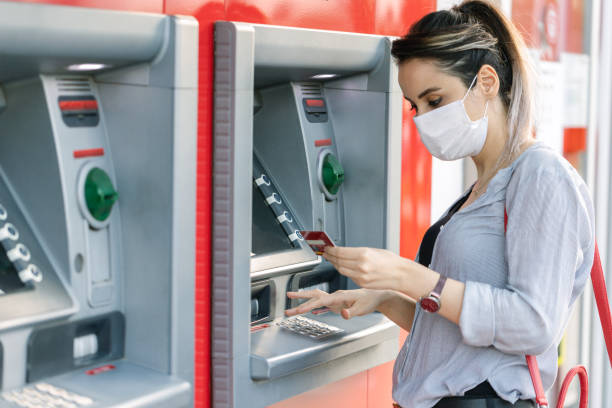 Young woman wearing protective face  mask while withdrawing money at ATM Young woman wearing protective face mask while withdrawing money at ATM banks and atms stock pictures, royalty-free photos & images