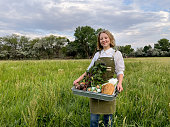 istock Young Woman With a Basket of Organic Produce, Milk, Eggs and other Groceries Posing Proudly in front of a Hayfield at Her Organic Retail Sustainable Farm 1325989310