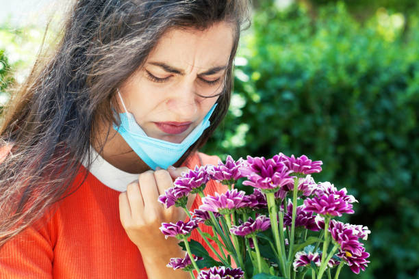 Young woman with a protective face mask smelling flowers stock photo