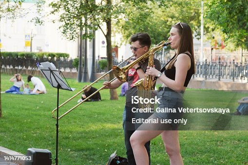 Young woman with a saxophone and a young man with a trumpet play in a city park