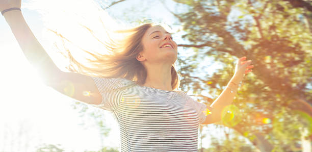 Young woman with arms outstretched. She is very happy and has the wind in her hair. She is carefree and is back lit with lens flare. Freedom concept.