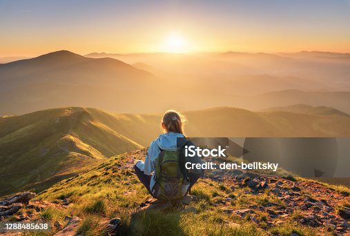 istock Young woman with backpack sitting on the mountain peak and beautiful mountains in fog at sunset in summer. Landscape with sporty girl, green forest, hills , sky, sunbeams. Travel and tourism. Yoga 1288485638
