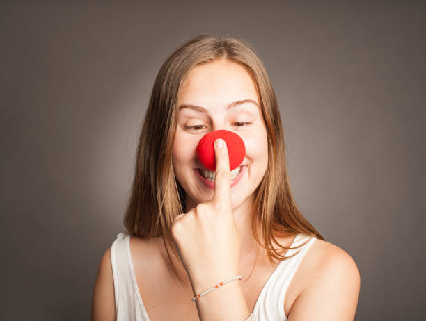 young woman with clown nose young woman with clown nose on a grey background clown's nose stock pictures, royalty-free photos & images