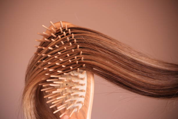 mujer joven con peine cepilla su cabello rubio - cabello humano fotografías e imágenes de stock