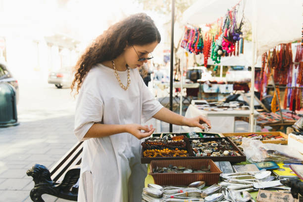 Young woman with curly hair shopping at flea market during bright sunny day Young woman student in eyeglasses spend the weekend shopping at the old flea market flea market photos stock pictures, royalty-free photos & images
