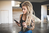 Portrait of young tattooed woman with blond dreadlocks texting message on mobile phone