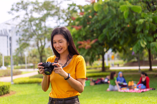 female photographer taking photos outdoor in public park, with people picnic at background