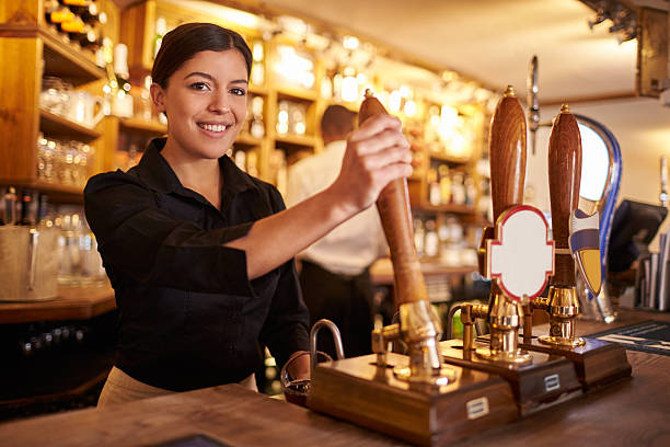 A young woman working behind a bar looking to camera, horizontal A young woman working behind a bar looking to camera, horizontal bartending stock pictures, royalty-free photos & images