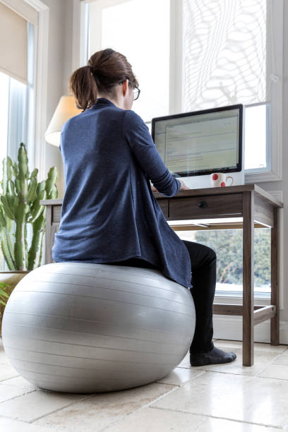 Young Woman Working From Home Young Woman Working From Home And using a fitness ball as chair yoga ball work stock pictures, royalty-free photos & images