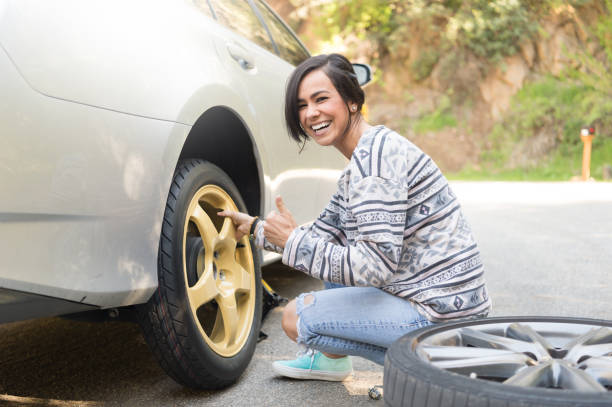 jeunes femmes changer un pneu crevé - femme tire photos et images de collection