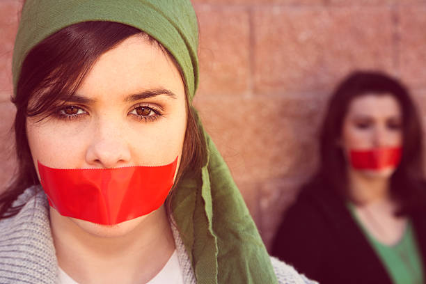young women with red tape over mouths in protest - plakband mond stockfoto's en -beelden