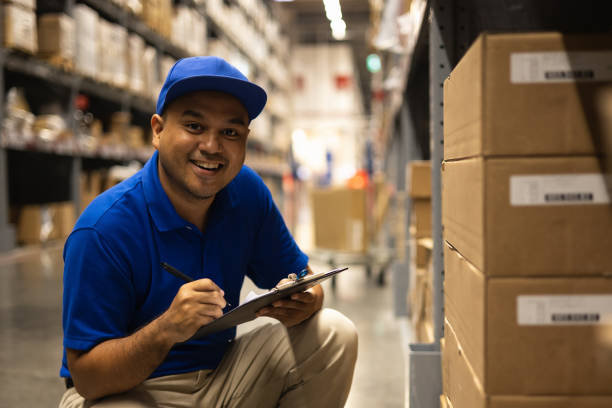 Young worker in blue uniform checklist manage parcel box product in warehouse. Asian man employee holding clipboard working at store industry. Logistic import export concept. stock photo