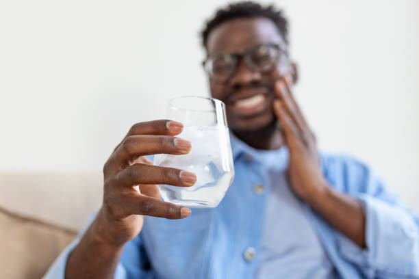 Youngcman with sensitive teeth and hand holding glass of cold water with ice. Healthcare concept. man drinking cold drink, glass full of ice cubes and feels toothache, pain stock photo