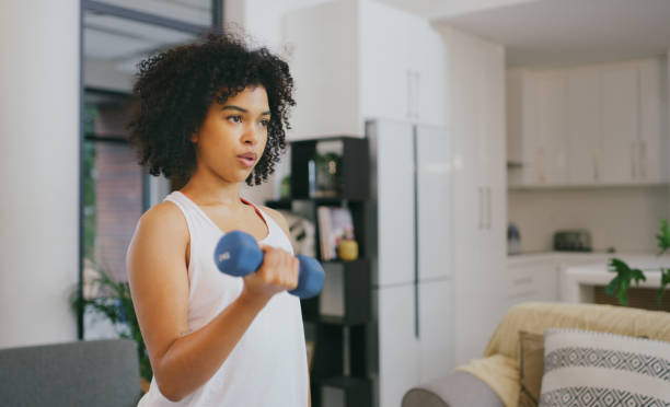 Your body won't go where your mind doesn't push it Shot of a young woman exercising with dumbbells at home curly hair stock pictures, royalty-free photos & images