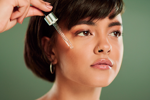 Cropped shot of a beautiful young woman holding a serum dropper against her face