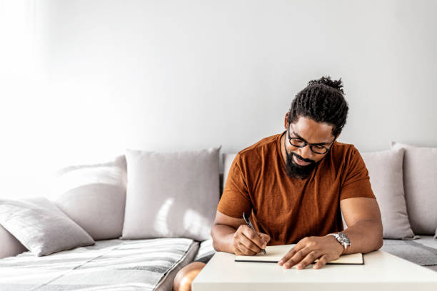 Your work ethic speaks volumes about you in business Image of happy African man with notepad and pen sitting on sofa. diary stock pictures, royalty-free photos & images
