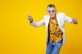 Funny and extravagant senior man dancing on coloured background