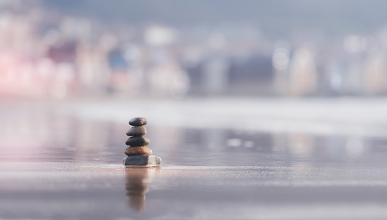 Zen like concept,Pebble tower rock stacked on top of each other by the sea on beach sand with blurry background,Stones pyramid is symbolizing, stability, harmony balance with shallow depth of field.