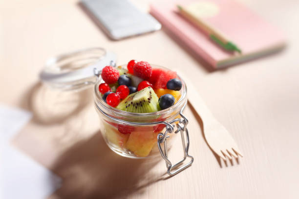 Zero Waste Lunch Fruits Salad in a Glass Container Fruits salad in a glass container with wooden fork in the office. snack stock pictures, royalty-free photos & images