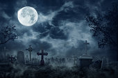 Zombie Rising Out Of A Graveyard cemetery In Spooky dark Night full moon. Holiday event halloween concept.
