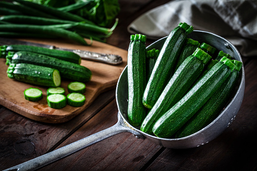 Fresh organic zucchini in an old metal colander shot on rustic wooden table. This vegetable is considered a healthy salad ingredient. Predominant colors are green and brown. Low key DSRL studio photo taken with Canon EOS 5D Mk II and Canon EF 100mm f/2.8L Macro IS USM