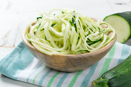 Raw zucchini spaghetti in a rustic wooden bowl on white table