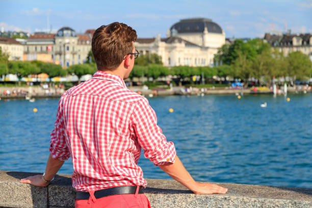 Zurich lake view Beautiful young man in traditional clothing looks out over lake Zurich (Zurichsee) on a summer day in Zurich, Switzerland Check Shirt Style pool stock pictures, royalty-free photos & images