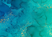 istock Background with turquoise blue watercolor waves or fluid art in alcohol ink style with golden splashes. 1286095893