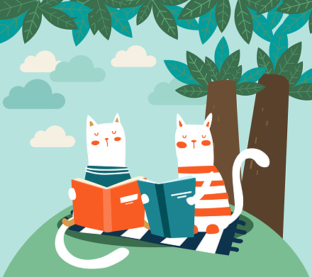 Cute cat reads a book under the tree. Funny animal relaxing in park