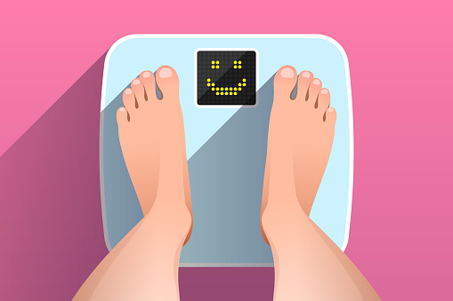 Feet of woman standing on bathroom scales with happy face on display