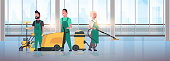 janitors team cleaning service concept cleaners in uniform working together with professional equipment modern hall interior panoramic windows cityscape background flat full length horizontal vector illustration