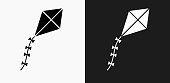 Kite Icon on Black and White Vector Backgrounds. This vector illustration includes two variations of the icon one in black on a light background on the left and another version in white on a dark background positioned on the right. The vector icon is simple yet elegant and can be used in a variety of ways including website or mobile application icon. This royalty free image is 100% vector based and all design elements can be scaled to any size.