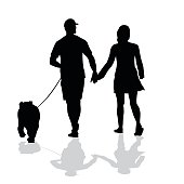 A vector silhouette illustration of a young couple walking hand in hand while taking their bulldog for a walk.